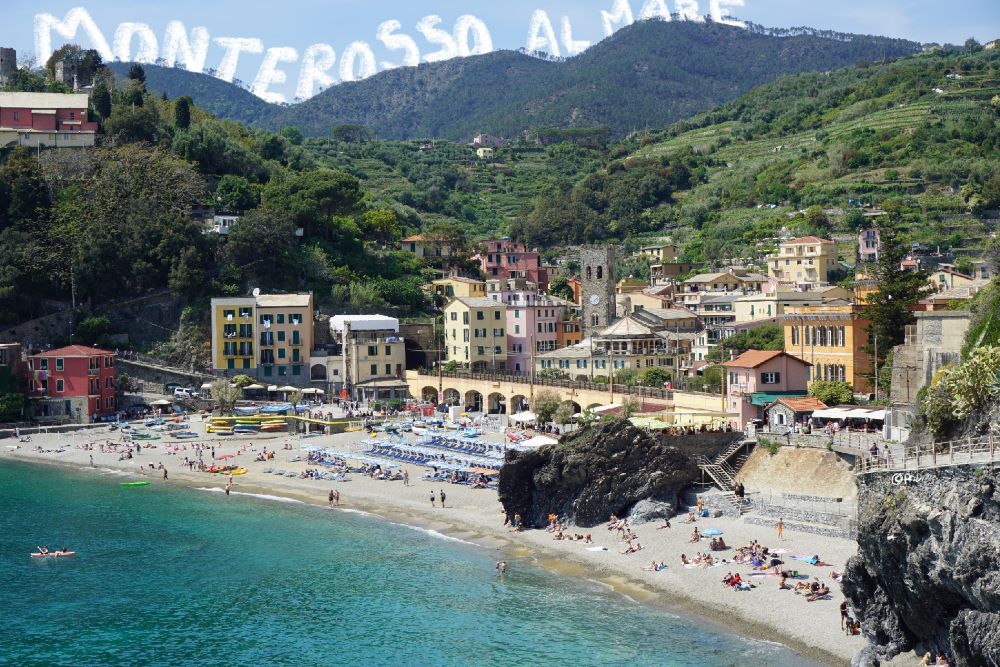 beach filled with blue umbrellas and Mediterranean buildings in Monterosso al Mare