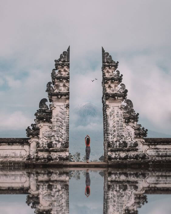 Woman standing in the heavenly pura lempuyang gates, ancient stone carvings on a balinese temple with mirrored reflection underneath pura lempuyang