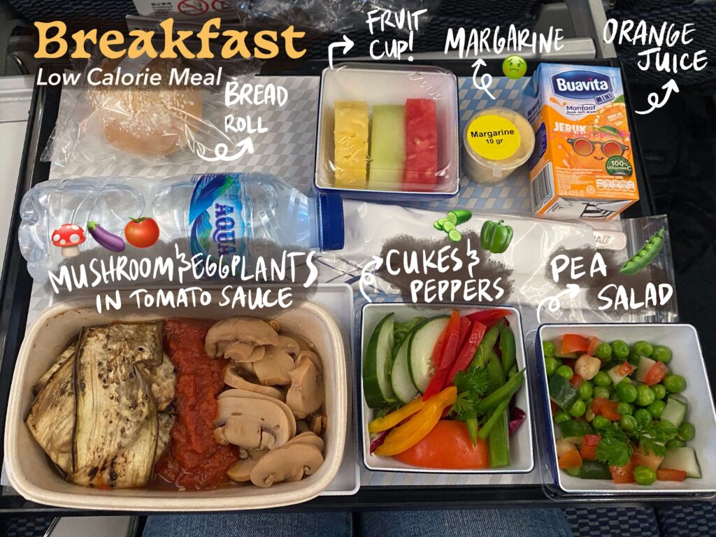 Breakfast low calorie meal at ANA Airlines Japan Jakarta to Tokyo. Mushroom and eggplants with tomato sauce, cucumber and pepper salad, pea salad, fruit slices, bread roll with margarine, orange juice