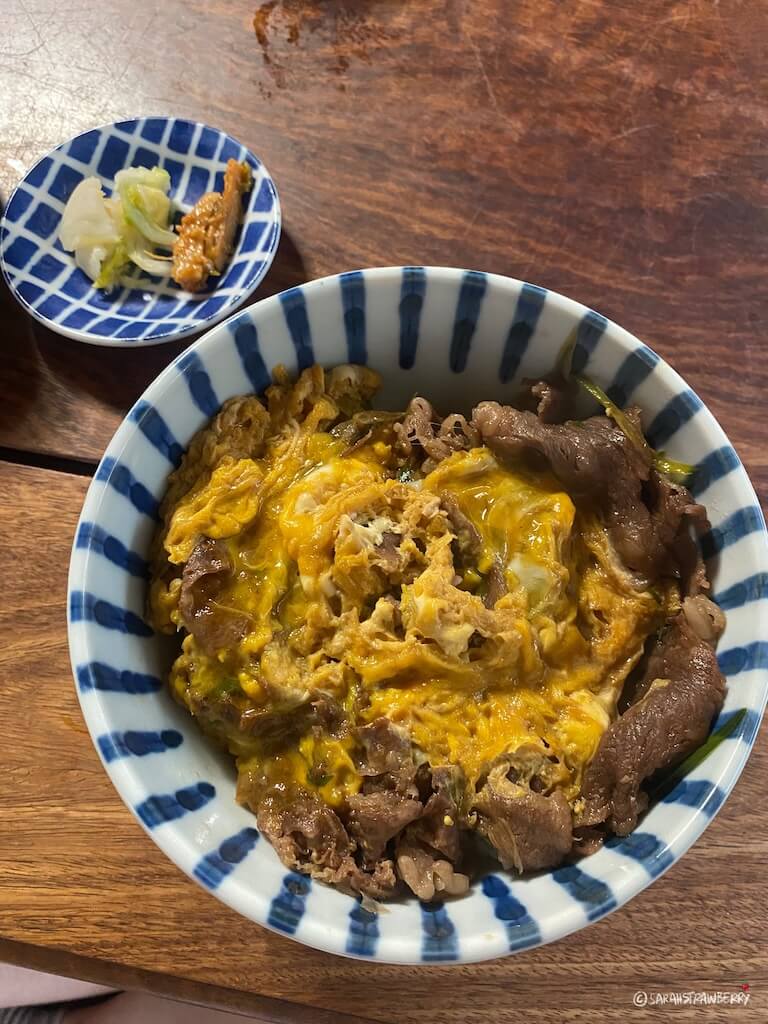 a rice bowl with beef and egg topping and cabbage pickles on the side